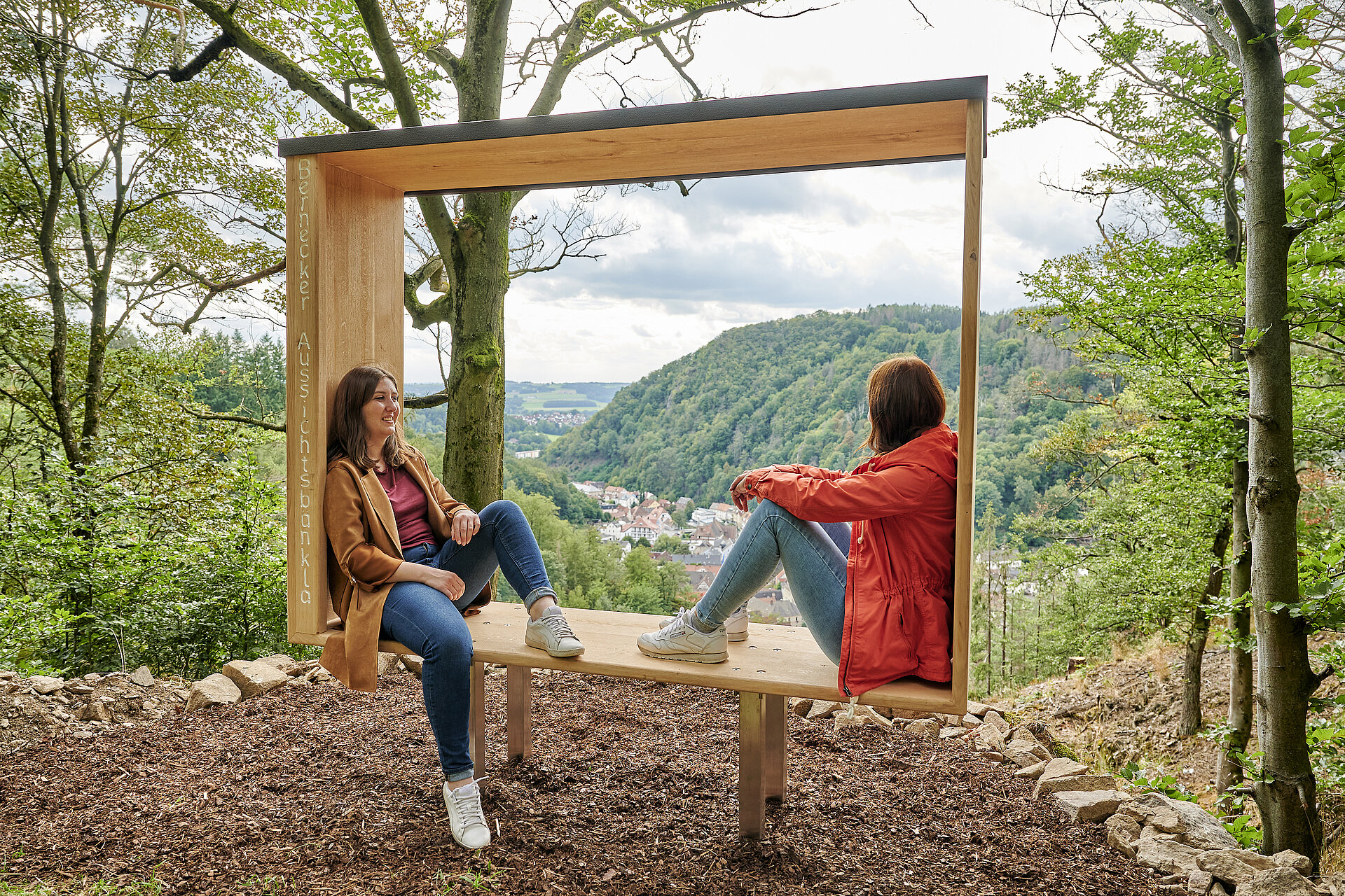 Zwei Frauen sitzen im großen Holzrahmen mit Blick auf Bad Berneck. 