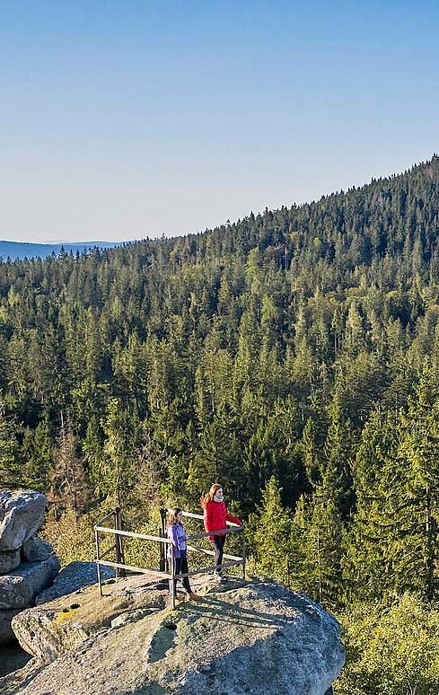 Zwei Menschen stehen auf dem Haberstein und blicken über Waldflächen zur Kösseine