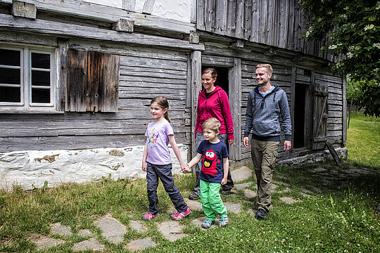 Zwei Kinder und zwei erwachsene verlassen ein Holzhaus im Freilichtmuseum