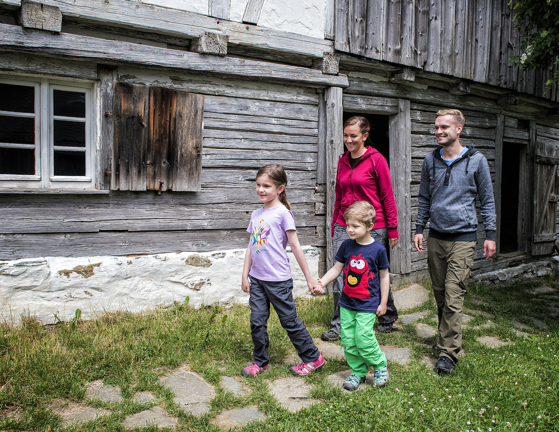 Zwei Kinder und zwei erwachsene verlassen ein Holzhaus im Freilichtmuseum