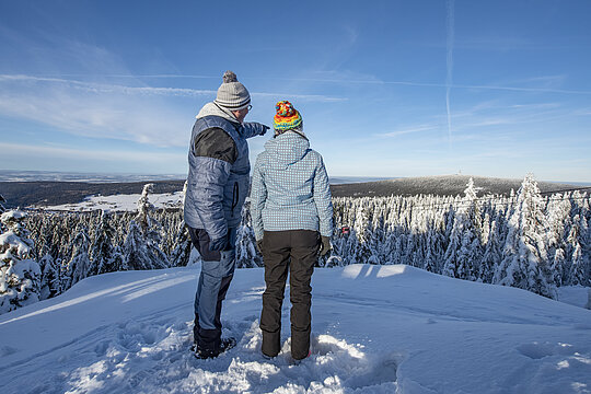 Zwei Personen blicken in die verschneite Winterlandschaft auf den Schneeberg