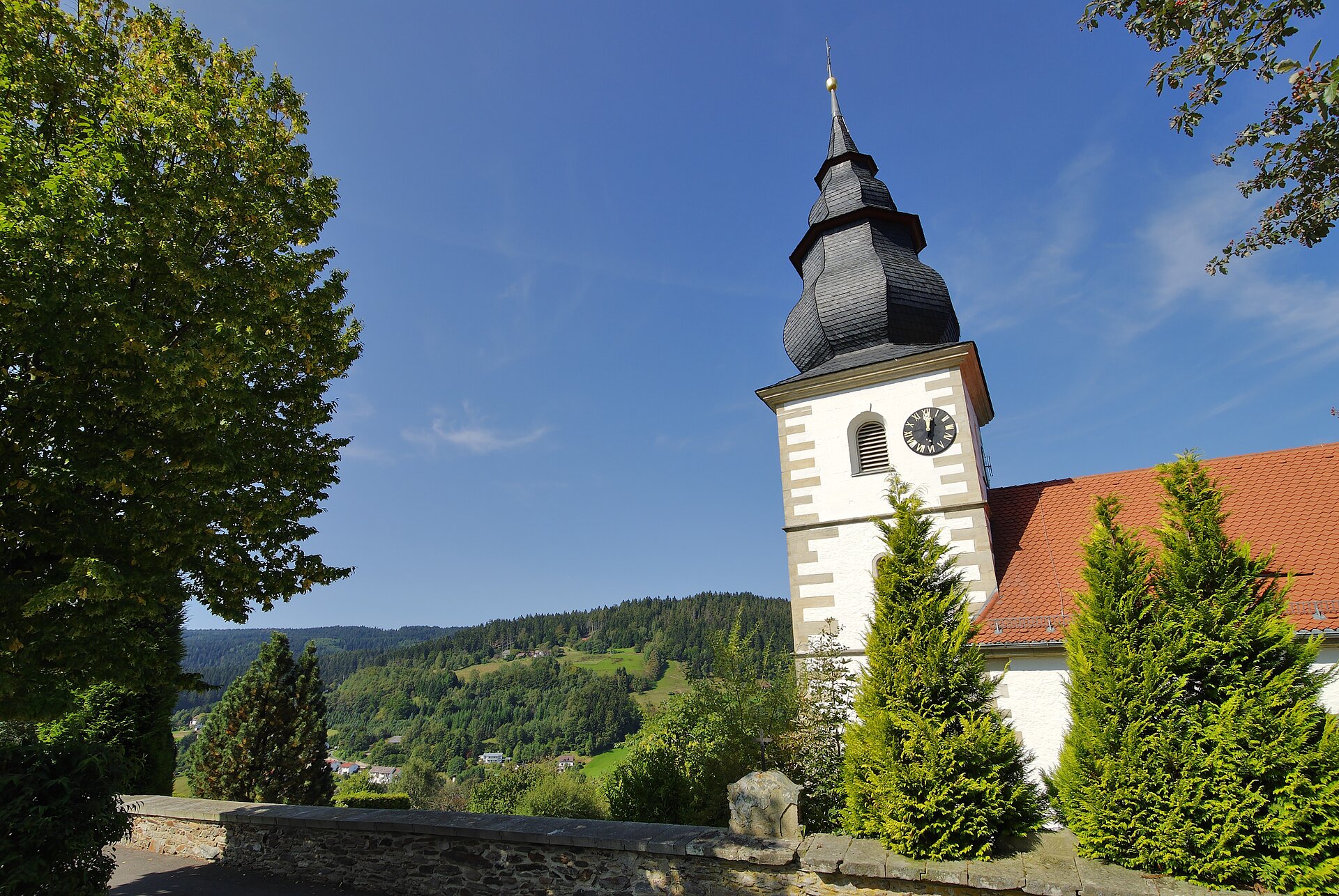 Blick auf die Kirche, im Hintergrund Wald und blauer Himmel