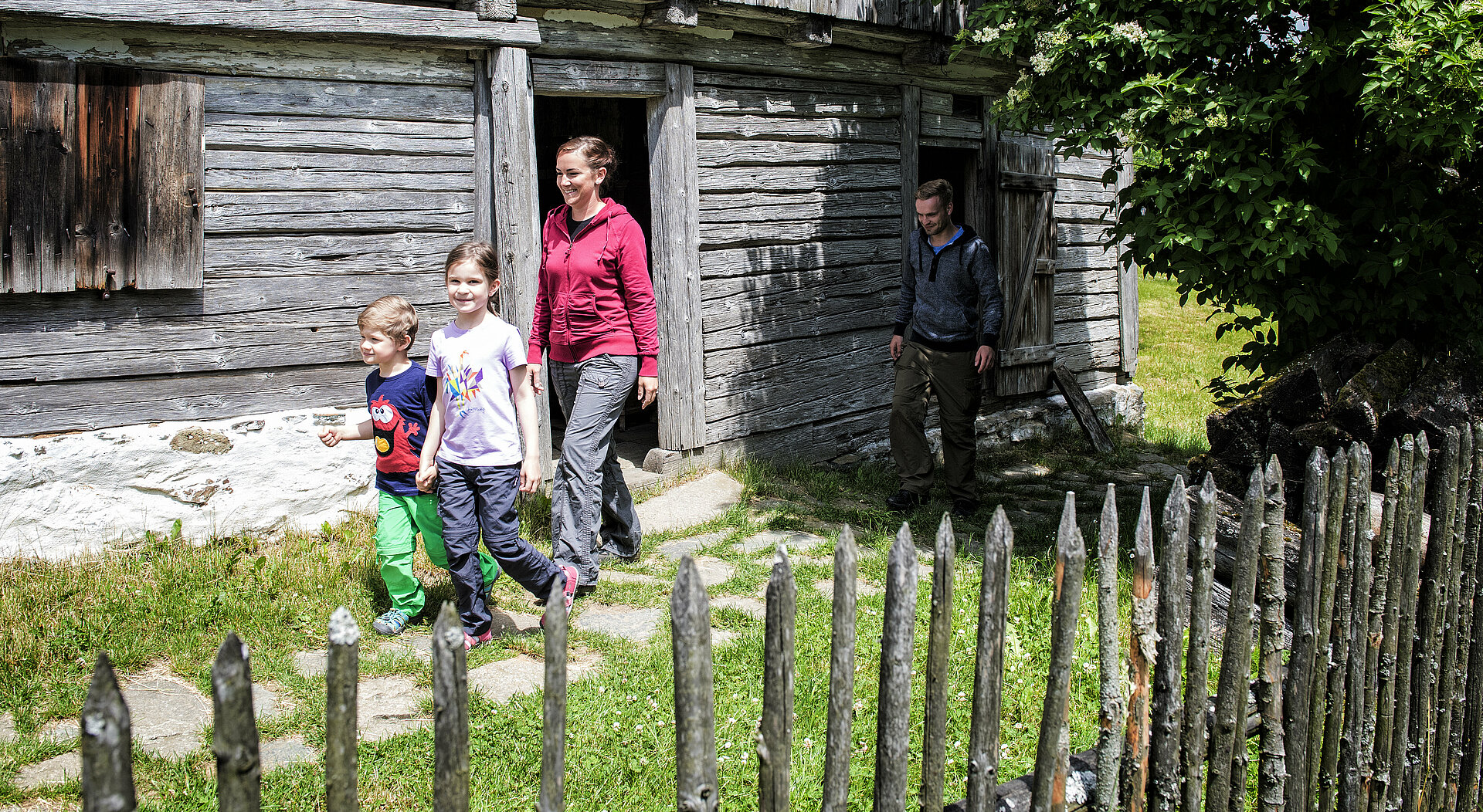 Zwei Kinder und eine Frau kommen gerade aus einem alten Holzhaus im Freilichtmuseum